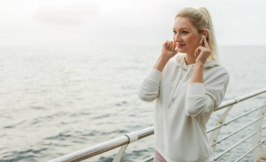 Kumsalda neşeli sarışın bir sporcunun portresi. Genç, sıska kadın kulaklıkla müzik dinliyor.