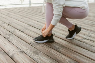 Kadın koşucu, plajda ayakkabılarını bağlayıp koşuya hazırlanıyor. Sağlıklı yaşam tarzı