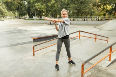 Açık havada antrenman yapmadan önce genç sarışın kadın ısınıyor. Aerobika