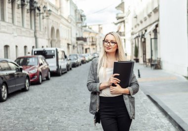 Şehir sokağında elinde klasörle kendine güvenen bir iş kadınının portresi