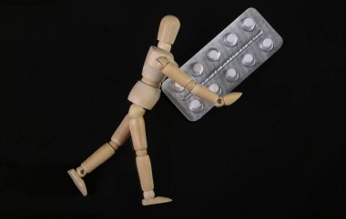 Tahta kukla mankeni, siyah arka planda izole edilmiş hapların su toplamasını tutuyor.