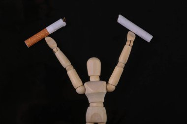 Ahşap kukla mankeni siyah arka planda izole edilmiş bir sigarayı kırar. Sigarayı bırakma kavramı