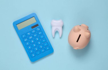 Dental treatment costs. Piggy bank, calculator and tooth on blue background. Top view clipart
