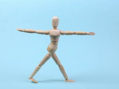 Ahşap kukla yoga yapıyor. Asana pozu mavi arka planda izole edilmiş.