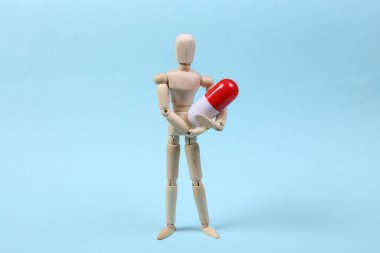 Ahşap bir kukla mavi arka planda kapsül hapı tutuyor. Tıp konsepti