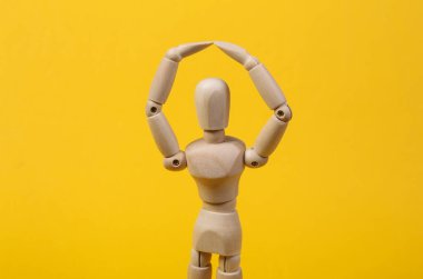 Tahta bir kukla kollarını başının üstünde tutuyor. Koruma konsepti. Sarıda izole edilmiş.