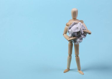 Mavi arka planda buruşmuş kağıt yumağı tutan tahta kukla.