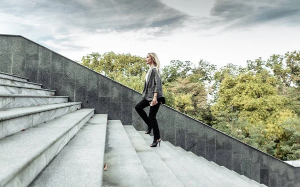 Purposeful, self-confident business lady climbs the stairs outdoors in cloudy weather. Career growth concept