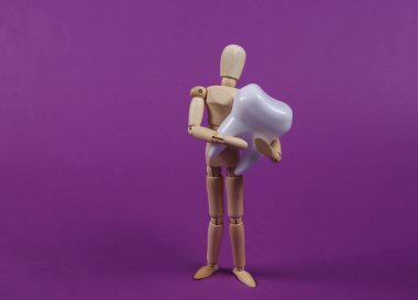 Ahşap kukla mankeni mor arka planda sahte bir diş tutuyor..