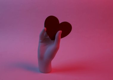 Manken eli kırmızı-mavi neon ışıkta kırmızı kalbi tutar. Minimalizm