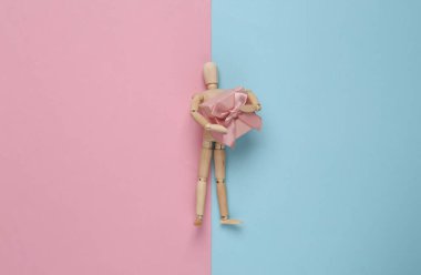 Ahşap kukla mankeni elinde pembe mavi pastel arka planda hediye kutuları tutuyor..