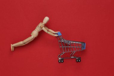 Ahşap kukla kırmızı arka planda süpermarket tramvayı yuvarlıyor. Alışveriş konsepti. Üst görünüm
