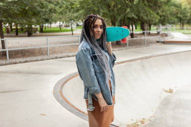 Parlak makyajlı sıradışı bir patenci ve kaykay alanında elinde bozuk para tutan Afrikalı bir kadın.