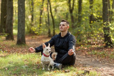Spor adamı, sonbahar ormanında evcil bir köpekle lotus pozisyonunda meditasyon yapar..
