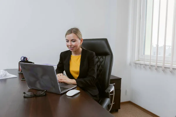 Business woman communicates by video conference while looking into a laptop while sitting at a table in her office. Online conference, Video call