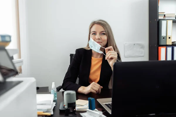 Business woman takes off the medical mask from her face in the office.