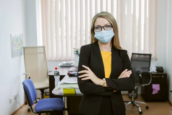 Confident business woman in medical mask stands in the office