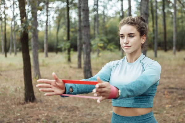 Young fitness woman with curly hair working out with fitness rubber bands in the forest