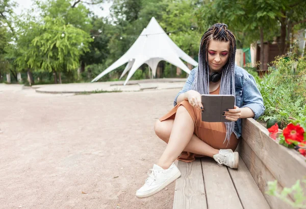 Extraordinary woman student millennial with african pigtails looks in tablet outdoors