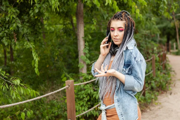 Extraordinary woman student millennial with african pigtails talking on phone outdoor