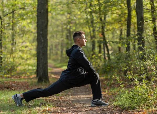 Active sport man trains warm-up exercises or stretching in the autumn forest. Healthy lifestyle. Outdoor workout