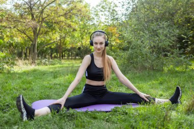 Paspasın üzerinde oturan sıska bir kadın ve parkta kulaklıkla müzik dinleyen. Sağlıklı yaşam tarzı