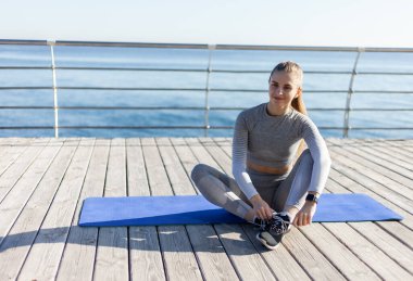 Güneşli bir günde plajda bir hasırda otururken bağcıklarını bağlayan zinde bir kadın. Sağlıklı yaşam tarzı