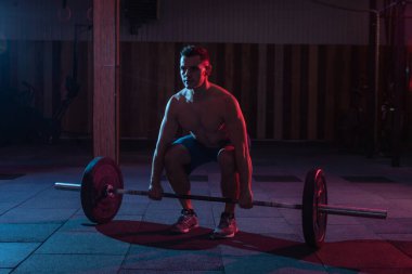 Spor salonunda ağırlık kaldırarak antrenman yapmak. Kaslı, güçlü bir adam, ağır bir halterle, kırmızı neon ışıklı kaldırma yapıyor.