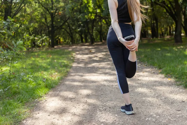 Active fit slim woman runner in sportswear stretches her legs in the park. Healthy lifestyle