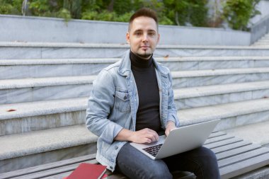 Genç bir öğrenci dizüstü bilgisayarla oturuyor. Beyaz adam dışarıda defter ile çalışıyor ya da çalışıyor..