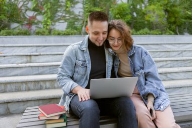 İki genç öğrenci dışarıda dizüstü bilgisayarla ders çalışıyor.