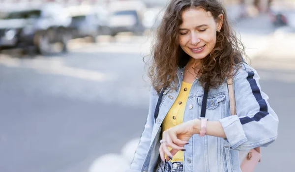 Wanita Rambut Keriting Ceria Dalam Jaket Denim Lihat Jam Tangan — Stok Foto