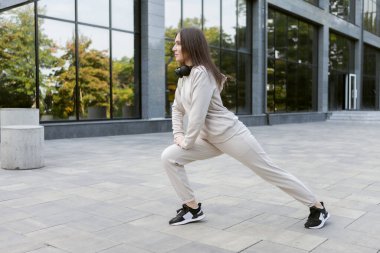 Açık havada çalışan zinde esmer bir kadın. Spor kıyafetlerindeki kadın sporcu kadın antrenmandan önce kollarını esnetiyor ya da ısıtıyor. Sağlıklı yaşam tarzı