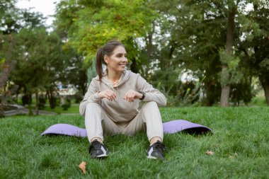 Çekici, fit bir kadın parkta paspasın üzerinde otururken dinleniyor. Fitness ya da dışarıda yoga.