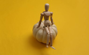 Sarı arka planda küçük beyaz balkabakları olan tahta kukla.