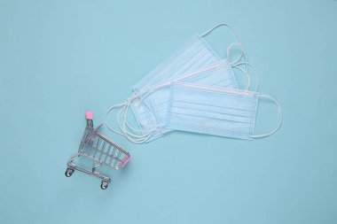 Mavi arka planda tıbbi maskeli alışveriş arabası.