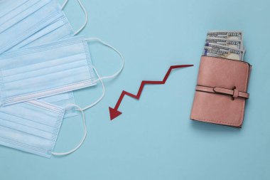 Tıbbi maskeler ve para dolu çanta. Düşen ok mavi arka planda aşağı bakıyor..