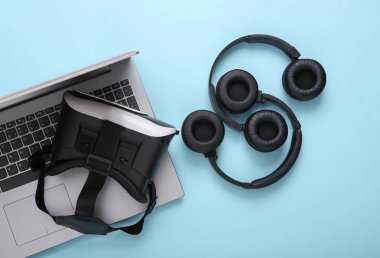 VR başlık ve iki çift siyah kablosuz kulaklık, mavi arka planda dizüstü bilgisayar. Modern aletler. Sanal bir gerçeklik