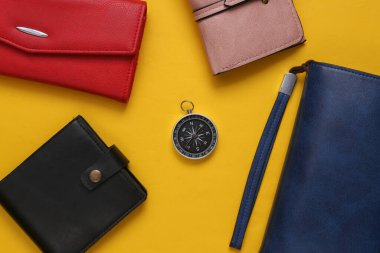 Sarı arka planda deri cüzdanlar ve pusula.