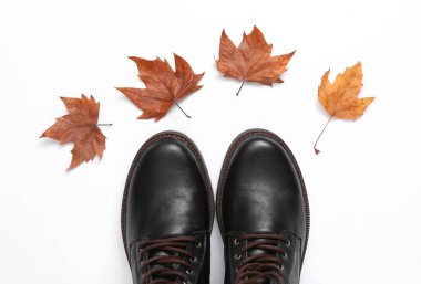 Erkek deri botları ve beyaz arka planda düşen sonbahar yaprakları