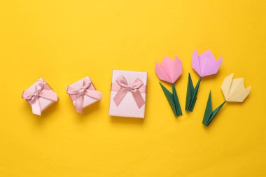 El yapımı origami laleleri ve sarı arka planda hediye kutuları. 8 Mart, kadınlar günü konsepti. Üst Manzara. Minimalizm