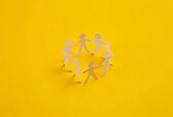 Cut paper human chain hold hands and show their unity on yellow background. Solidarity and peace