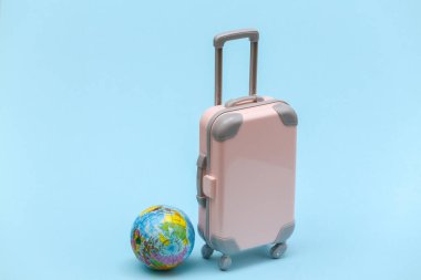 Uluslararası seyahat konsepti. Mini plastik seyahat valizi ve mavi pastel arka planda küre. Asgari biçim