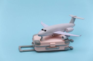 Hava yolculuğu konsepti. Mini plastik seyahat valizi ve mavi arka planda uçak..