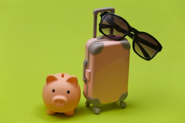 Seyahat ya da seyahat konsepti. Güneş gözlüklü mini plastik çanta ve yeşil arka planda kumbara..