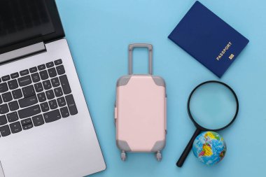 Tatil ve seyahat planlama konsepti. Laptop ve mini plastik seyahat valizi, dünya, mavi arka planda pasaport. Üst görünüm