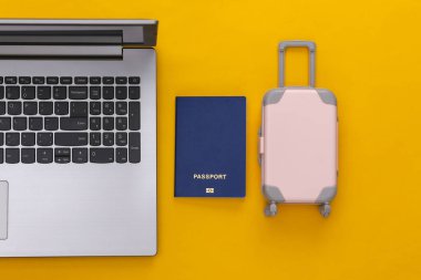 Tatil ve seyahat planlama konsepti. Laptop ve mini plastik seyahat çantası, sarı arka planda pasaport. Üst görünüm