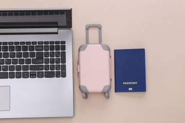 Tatil ve seyahat planlama konsepti. Laptop ve mini plastik seyahat çantası, bej arka planda pasaport. Üst görünüm
