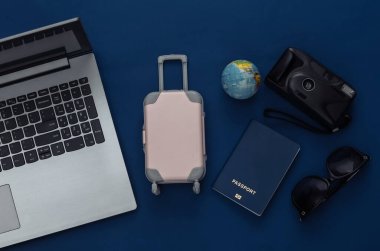 Tatil ve seyahat planlama konsepti. Klasik mavi arka planda dizüstü bilgisayar ve seyahat aksesuarları. Üst görünüm