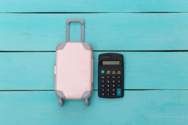 Tatil ve seyahat planlama konsepti. Mini plastik seyahat valizi, mavi ahşap arka planda hesap makinesi. Üst görünüm